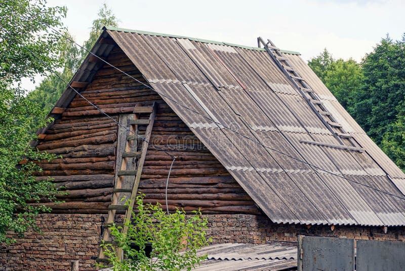 Part of an old country barn with a wooden gray attic under a slate roof with a ladder against the wall