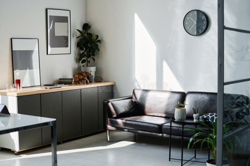 Part of spacious modern office with leather couch standing by wall with clock stock photos