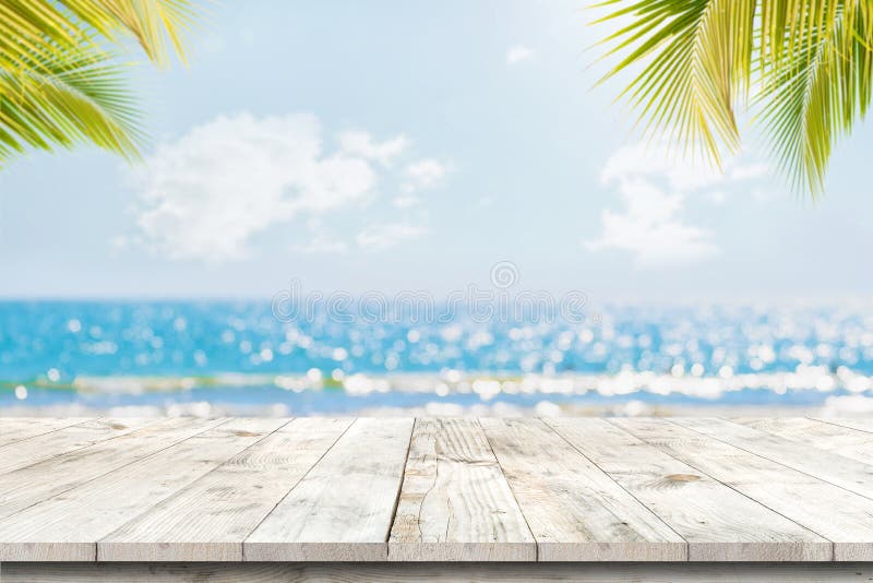 Parte superior da tabela de madeira com seascape e folhas de palmeira, da luz do bokeh do borrão do mar calmo e do céu no fundo t