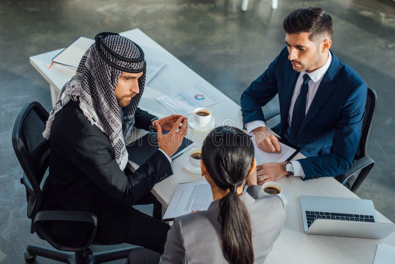 Multiethnic business partners and translator discussing contract on meeting in office. Multiethnic business partners and translator discussing contract on meeting in office