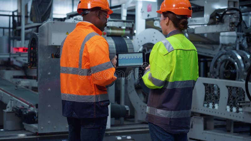 Parteneri concentrați care discută despre hărți pe un computer modern de tip tabletă la o fabrică uriașă. stock photo