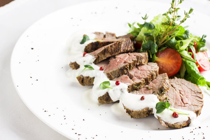 Partes de bifes da carne com molho e vegetais na placa branca imagem de stock Partes de bifes da carne com molho e vegetais na placa branca imagem de stock