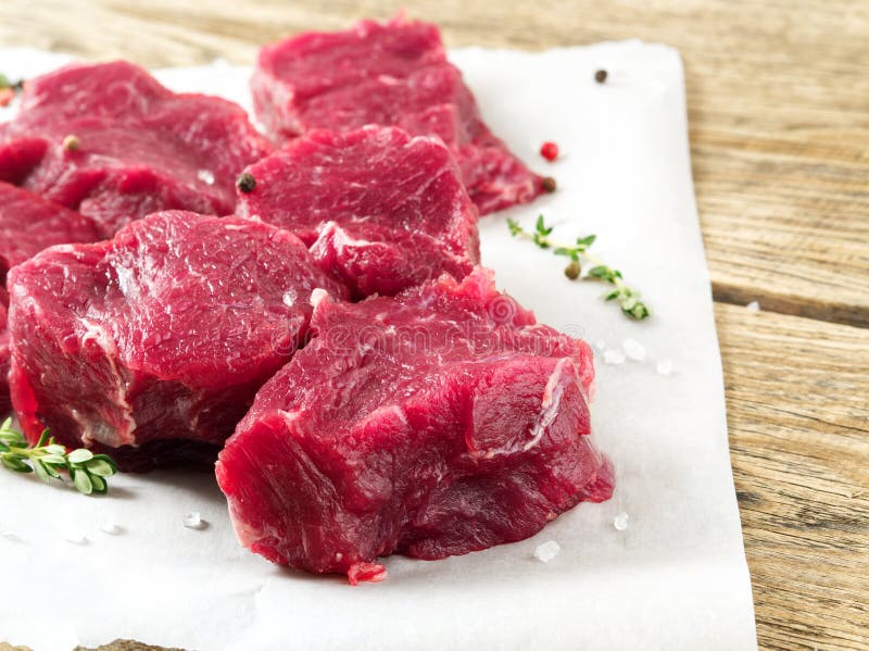 Parti di carne grezza Manzo crudo con le spezie sulla carta pergamena bianca su fondo rustico approssimativo di legno, vista late fotografia stock libera da diritti Parti di carne grezza Manzo crudo con le spezie sulla carta pergamena bianca su fondo rustico approssimativo di legno, vista late fotografia stock libera da diritti