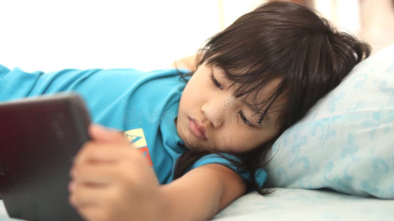 Partial view of Asian little girl using tablet in bed at home, mobile gadget addiction on children royalty free stock images