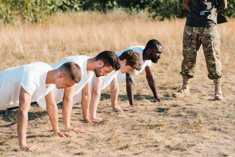 Partial View of Tactical Instructor Examining Multicultural Soldiers Doing Push Ups Stock Photo