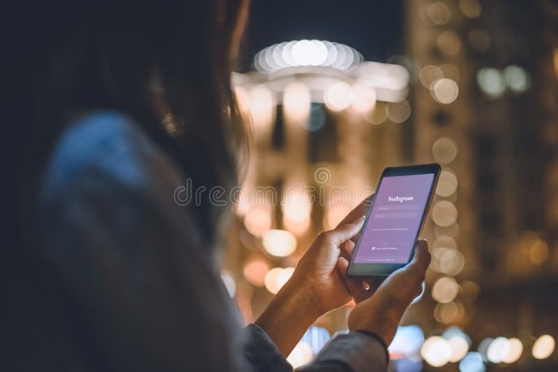 partial view of woman using smartphone with instagram logo on screen and night city lights on background