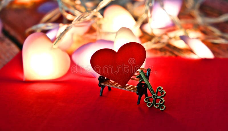 Partially blurred red heart on  mini bench and miniature key.  Key of my heart and  true love concept. In dark settings with retro