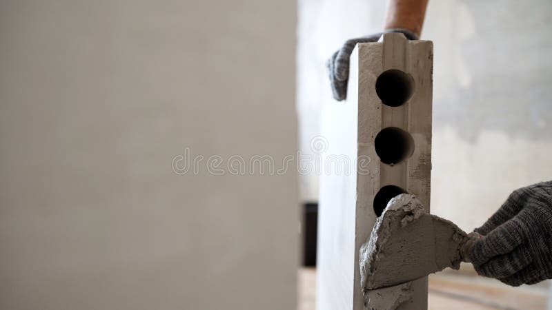 A mason applies cement adhesive to a brick when constructing an interior wall. Partition made of tongue-and-groove slabs. interior partition made of bricks under construction. A mason applies cement adhesive to a brick when constructing an interior wall. Partition made of tongue-and-groove slabs. interior partition made of bricks under construction