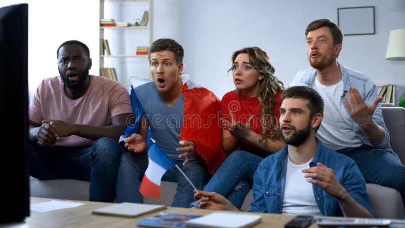 Partido de observación de los amigos franceses en la TV en casa, apoyando al equipo de fútbol preferido imagenes de archivo Partido de observación de los amigos franceses en la TV en casa, apoyando al equipo de fútbol preferido imagenes de archivo