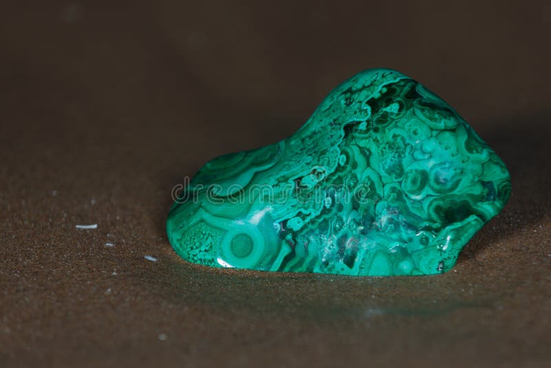 Partially polished Green free form Bullseye Malachite specimen on wet sand  in front of the lake at sunrise. Partially polished Green free form Bullseye Malachite specimen on wet sand  in front of the lake at sunrise.