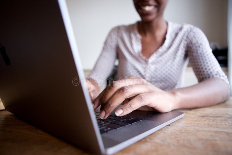Partisk stående av att le kvinnasammanträde på skrivbordet och maskinskrivning på bärbar datordatoren