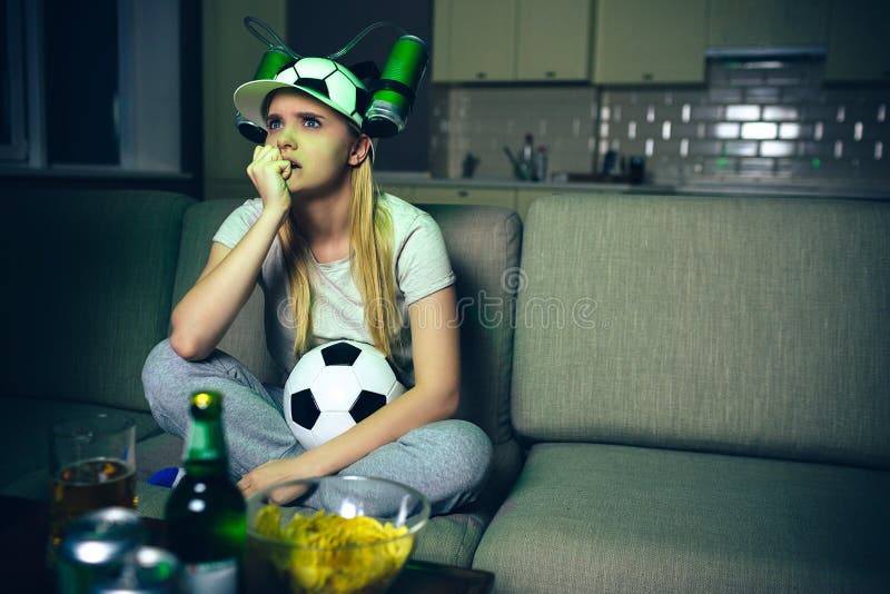 Partita di football americano dell'orologio della giovane donna sulla TV alla notte Il modello biondo infelice di ribaltamento si immagini stock Partita di football americano dell'orologio della giovane donna sulla TV alla notte Il modello biondo infelice di ribaltamento si immagini stock
