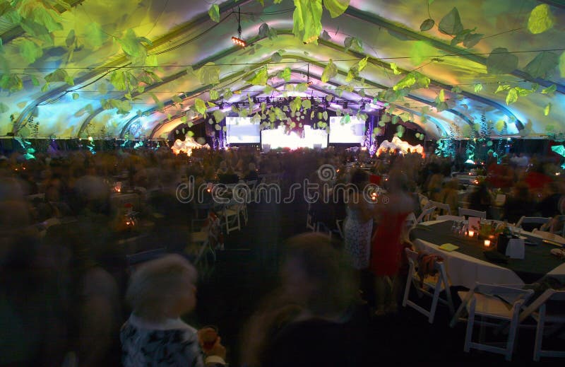 A large group of 800 people party room table set inside a tent with crowd of people. A large group of 800 people party room table set inside a tent with crowd of people