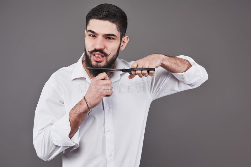 Pas plus de barbe Portrait de jeune homme beau coupant sa barbe avec des ciseaux et regardant l'appareil-photo tout en se tenant image stock Pas plus de barbe Portrait de jeune homme beau coupant sa barbe avec des ciseaux et regardant l'appareil-photo tout en se tenant image stock
