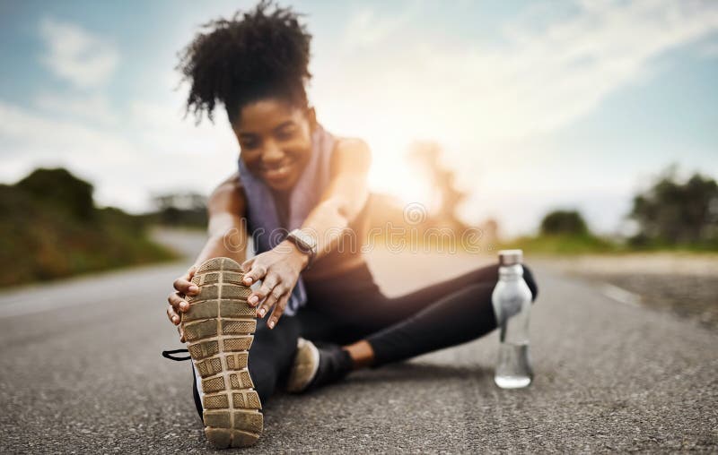 Pasar por su rutina de warmup. una joven deportista estirando sus piernas mientras hace ejercicio al aire libre. imagenes de archivo