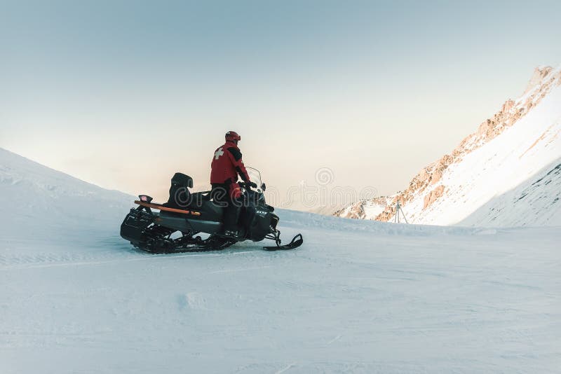 Paseos de la moto de nieve del salvavidas del hombre en las montañas foto de archivo libre de regalías Paseos de la moto de nieve del salvavidas del hombre en las montañas foto de archivo libre de regalías