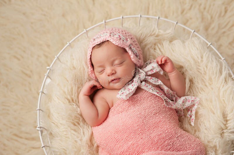 A portrait of a five week old newborn baby girl wearing a pink bonnet. She has a subtle smile and is peacefully sleeping in a wire basket. A portrait of a five week old newborn baby girl wearing a pink bonnet. She has a subtle smile and is peacefully sleeping in a wire basket.