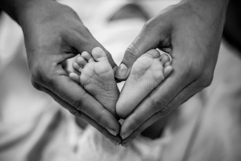 Pasgeboren babyvoeten moedershanden in zijn die als een hart worden gevormd. Moeder die haar liefde en affectie tonen. Zwart-wit