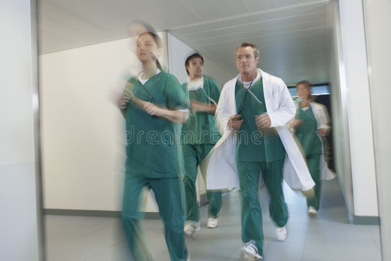 Pasillo del hospital de los doctores In Scrubs Running Through fotos de archivo libres de regalías Pasillo del hospital de los doctores In Scrubs Running Through fotos de archivo libres de regalías