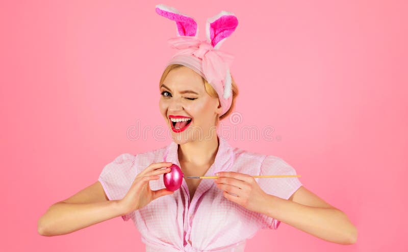 Pasqua felice. donna che fa l'occhiolino nelle orecchie di coniglio che decora le uova. coniglietto sorridente che dipinge un uovo immagine stock