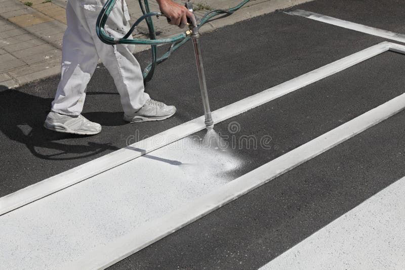 One adult worker spraying pedestrian crosswalk at a street using spraygun. One adult worker spraying pedestrian crosswalk at a street using spraygun