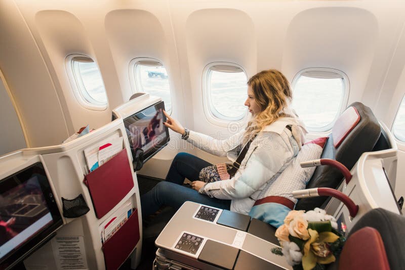 Woman passenger in business class of airplane. Information technologies and service in first class. Place with screen near the window. Woman passenger in business class of airplane. Information technologies and service in first class. Place with screen near the window