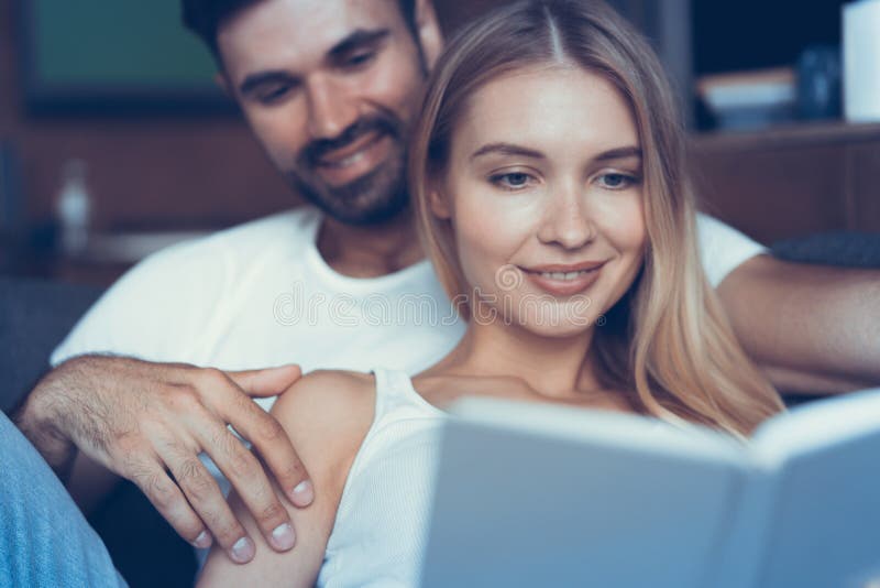 Passant le temps gentil à la maison Beaux jeunes couples affectueux collant entre eux et souriant tandis que femme tenant un livr photographie stock