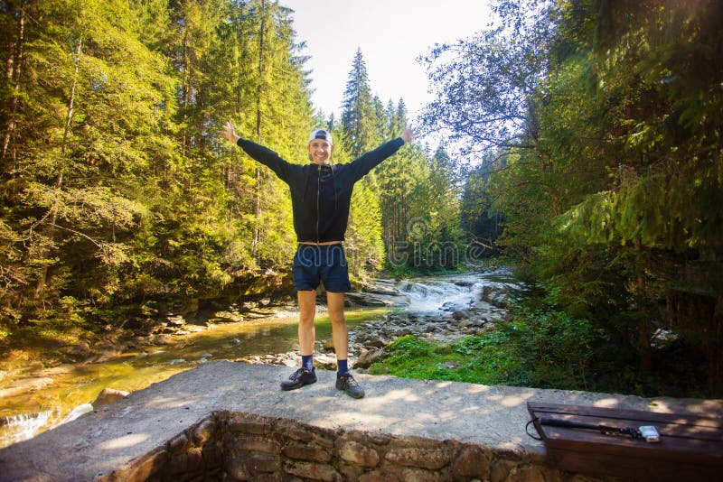 Passeggiata del giovane vicino al fiume veloce nel mezzo della foresta fotografia stock Passeggiata del giovane vicino al fiume veloce nel mezzo della foresta fotografia stock
