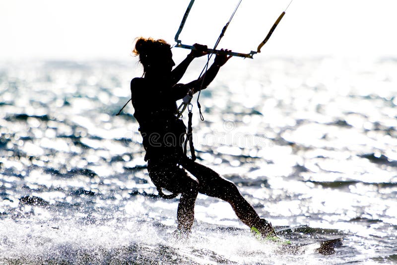 Passeios de um papagaio-surfista da jovem mulher contra o sol fotografia de stock Passeios de um papagaio-surfista da jovem mulher contra o sol fotografia de stock
