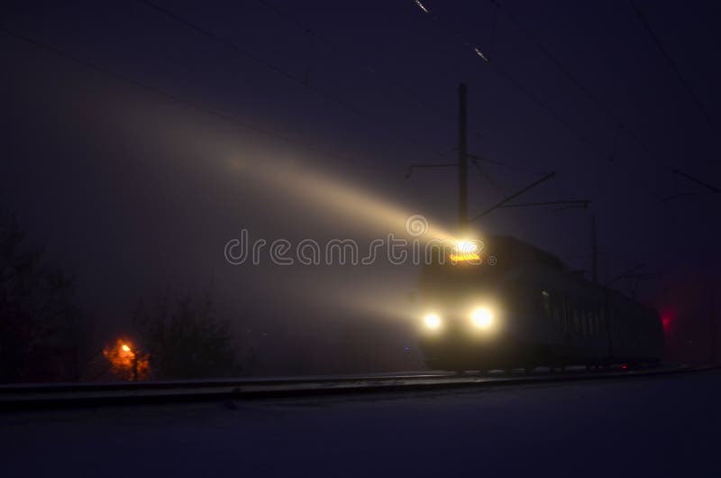 Passenger train in the fog, the light from the headlights in the night on the rail road.