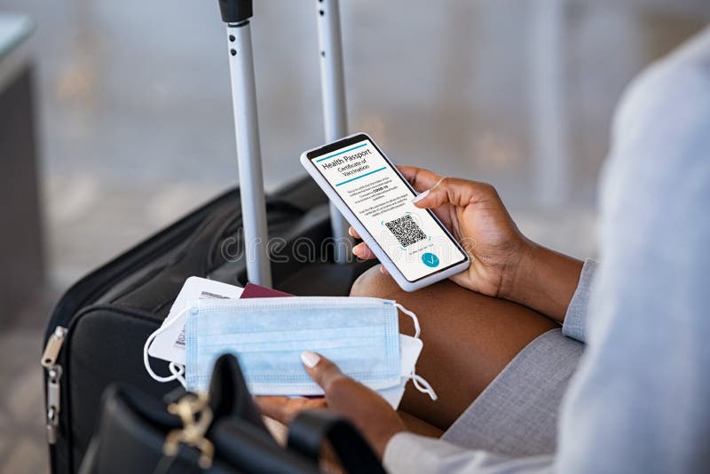 Close up of black hands of woman sitting in airport lounge checking her valid digital vaccination passport for covid19 while holding face mask and boarding pass. Businesswoman displaying  health passport for covid-19 while traveling during coronavirus pandemic. The health certificate indicates that the holder has been vaccinated against coronavirus covid-19 and is now able to travel. Close up of black hands of woman sitting in airport lounge checking her valid digital vaccination passport for covid19 while holding face mask and boarding pass. Businesswoman displaying  health passport for covid-19 while traveling during coronavirus pandemic. The health certificate indicates that the holder has been vaccinated against coronavirus covid-19 and is now able to travel