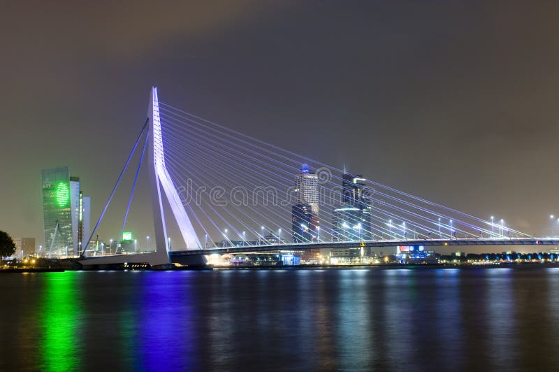 The famous Erasmus Suspension bridge with the Rotterdam skyline in the background at night, reflecting in the river Meuze. The famous Erasmus Suspension bridge with the Rotterdam skyline in the background at night, reflecting in the river Meuze