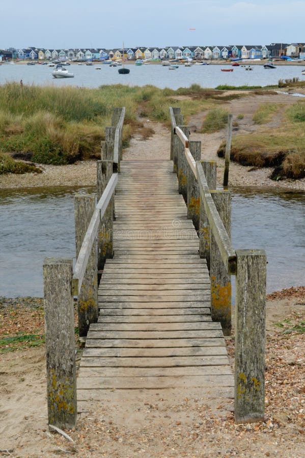 Passerelle à travers le courant avec la rangée des huttes de plage dans la distance photographie stock Passerelle à travers le courant avec la rangée des huttes de plage dans la distance photographie stock
