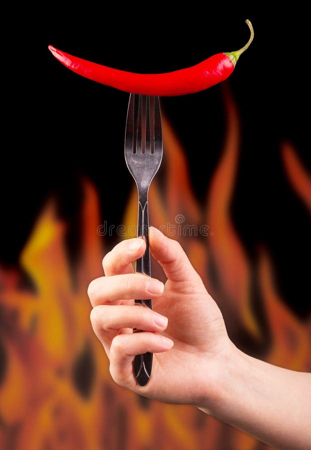 Passi la forcella della tenuta con peperoncino rosso sulle fiamme del fondo fotografia stock libera da diritti Passi la forcella della tenuta con peperoncino rosso sulle fiamme del fondo fotografia stock libera da diritti