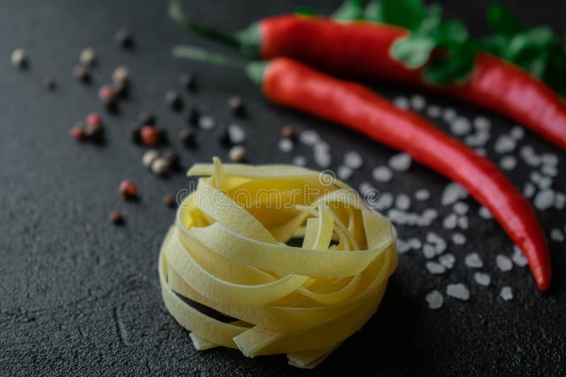 Pasta cruda del fettuccine su fondo nero con i ramoscelli freschi sale marino e granelli di pepe del coriandolo del peperoncino r fotografia stock Pasta cruda del fettuccine su fondo nero con i ramoscelli freschi sale marino e granelli di pepe del coriandolo del peperoncino r fotografia stock
