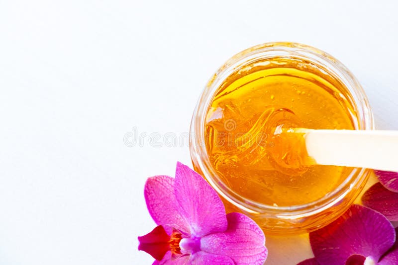 Depilation and beauty concept - sugar paste or wax honey for hair removing with wooden waxing spatula stick in jar on flower background. copyspase. Depilation and beauty concept - sugar paste or wax honey for hair removing with wooden waxing spatula stick in jar on flower background. copyspase