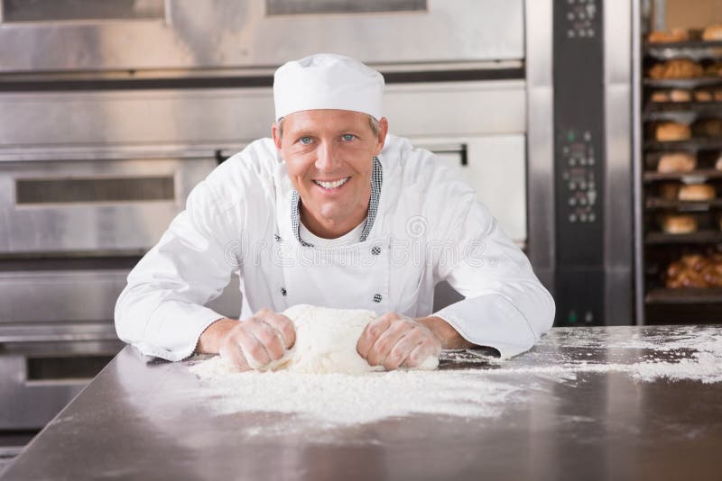 Smiling baker kneading dough on counter in the kitchen of the bakery. Smiling baker kneading dough on counter in the kitchen of the bakery