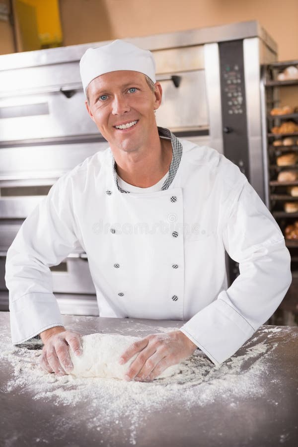 Smiling baker kneading dough on counter in the kitchen of the bakery. Smiling baker kneading dough on counter in the kitchen of the bakery