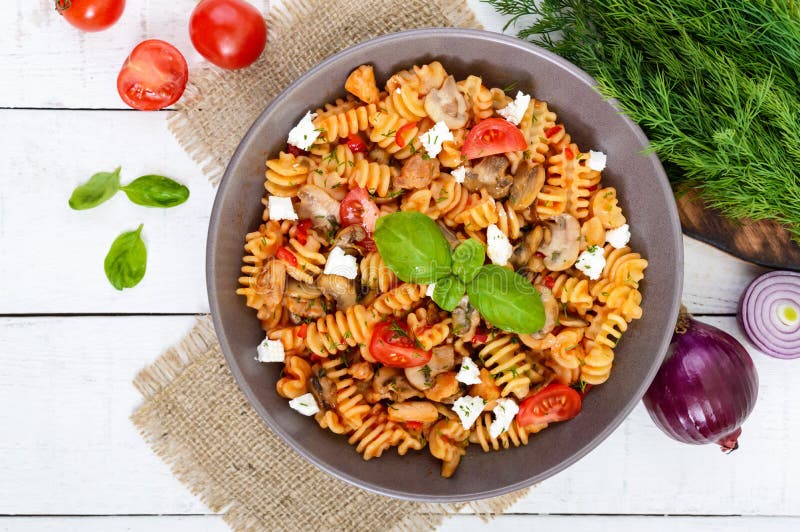 Pasta Radiatori with chicken, mushrooms, cherry tomatoes, feta cheese and tomato sauce on a white wooden background.