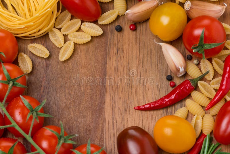 Pasta, spices and cherry tomatoes on wooden board