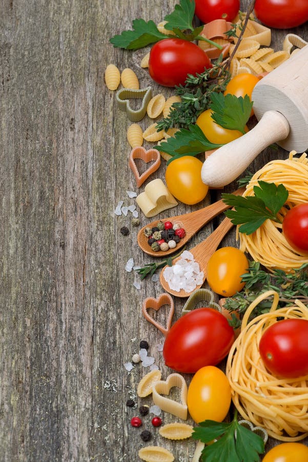 Pasta, spices, herbs and tomatoes on a wooden background