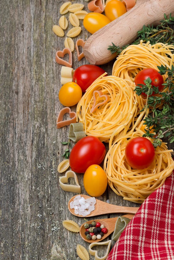Pasta, tomatoes and spices on wooden background, top view