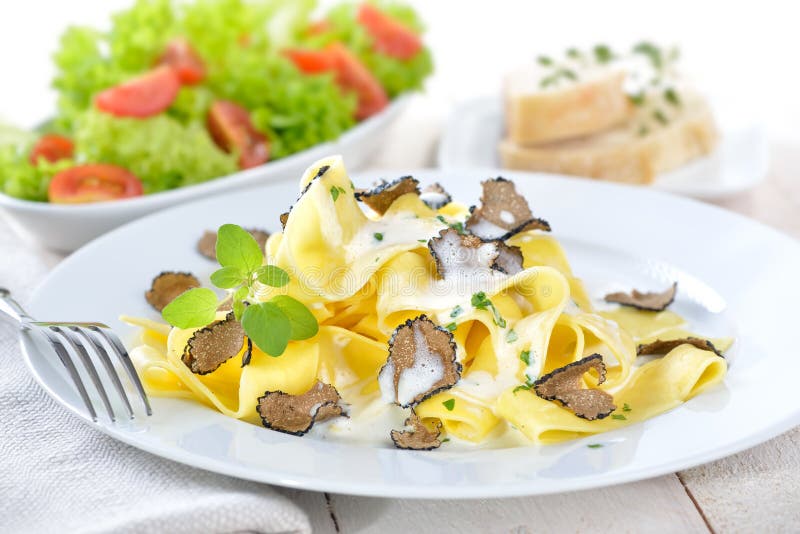 Italian papardelle with fresh black autumn truffles and cream sauce, in the background a mixed side salad and slices of baguette. Italian papardelle with fresh black autumn truffles and cream sauce, in the background a mixed side salad and slices of baguette