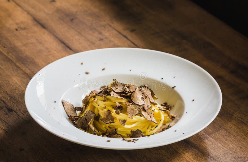 Pasta with truffles in white plate.Tagliatelle with black truffle on wooden table. Pasta with truffles in white plate.Tagliatelle with black truffle on wooden table.