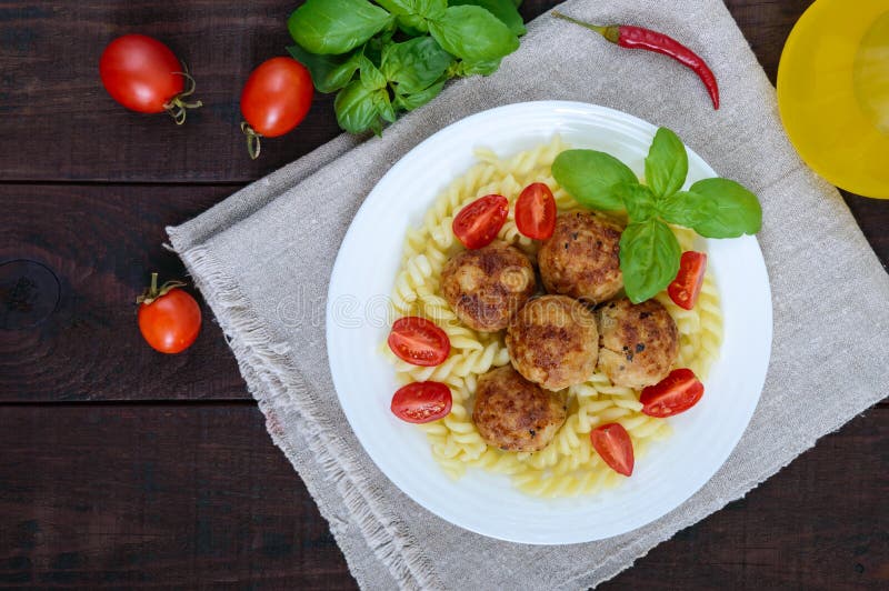 Pastafutsilli med köttbollar, körsbärsröda tomater, basilika på en vit platta på en mörk träbakgrund royaltyfria bilder Pastafutsilli med köttbollar, körsbärsröda tomater, basilika på en vit platta på en mörk träbakgrund royaltyfria bilder