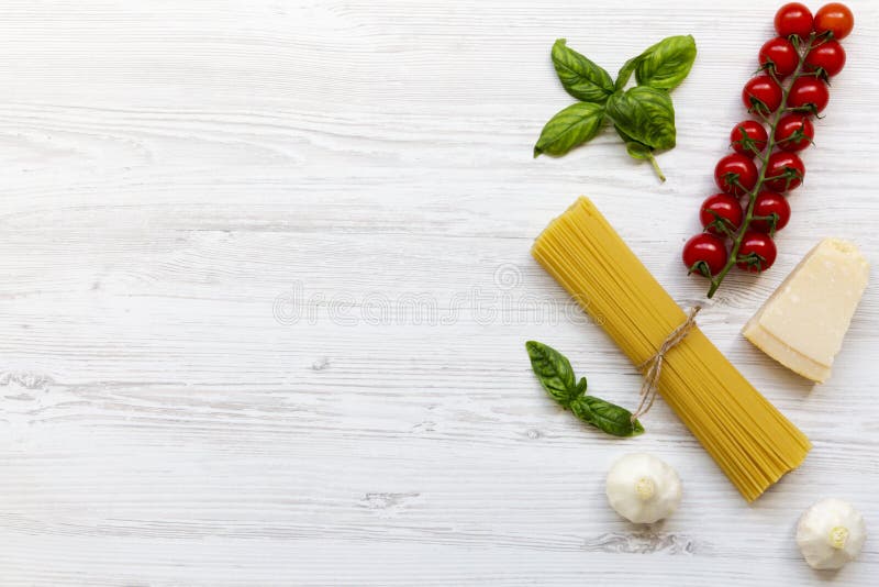 Pastaingredienser: spagetti, ostparmesan, vitlök och tomater med basilika på vit träbakgrund, royaltyfri foto Pastaingredienser: spagetti, ostparmesan, vitlök och tomater med basilika på vit träbakgrund, royaltyfri foto