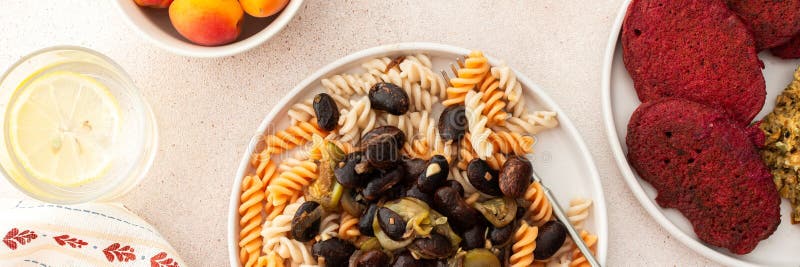 Paste alimentari prive di glutenzioni con fagioli al forno e zucchine a fianco di pancake di barbabietole con hummus di girasole immagini stock libere da diritti