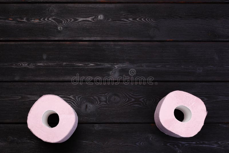 Pastel pink toilet paper rolls on black wooden background Stock