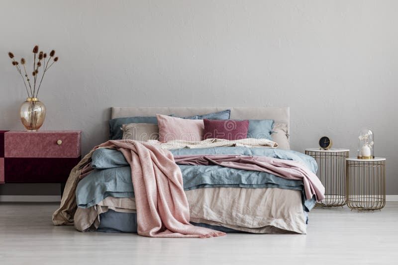 Pastel roze, beige en blauw beddengoed op bed ter grootte van de koning in de slaapkamer, kopieerruimte op lege grijze wand