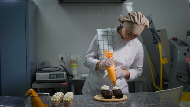 Pasteles femeninos que exprimen suavemente la crema poner crema blanca de la leche de un bolso de la comida para las magdalenas c